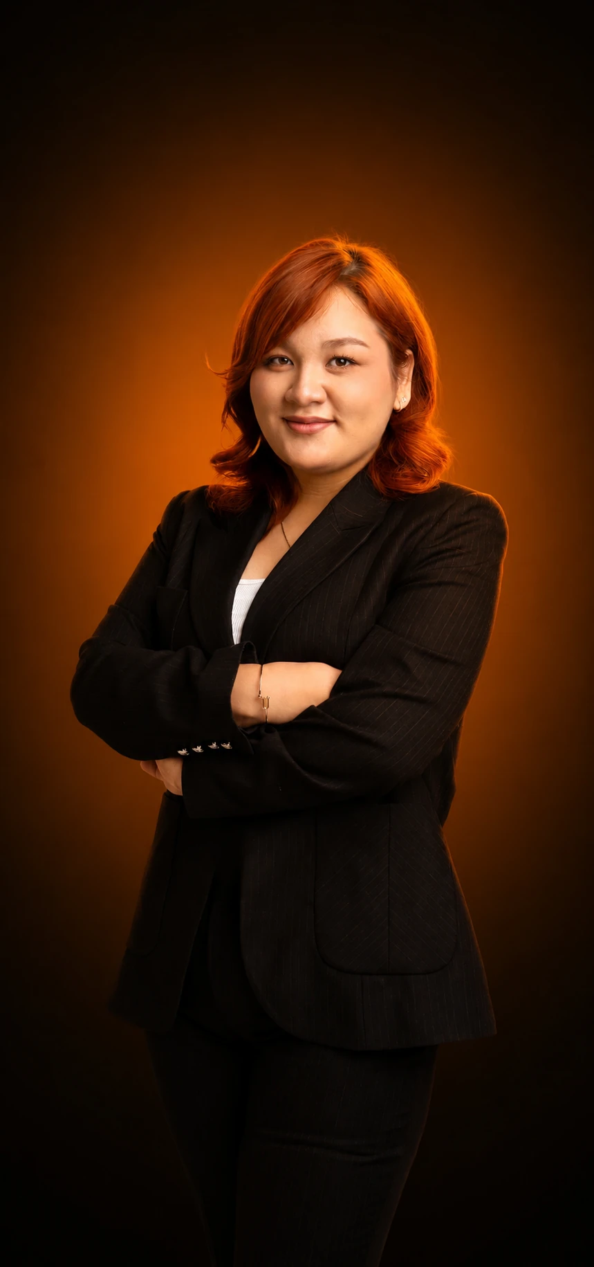 Muhayyo Rahmatxonova in a black suit, photographed against a dark studio backdrop lit by a warm rim light.